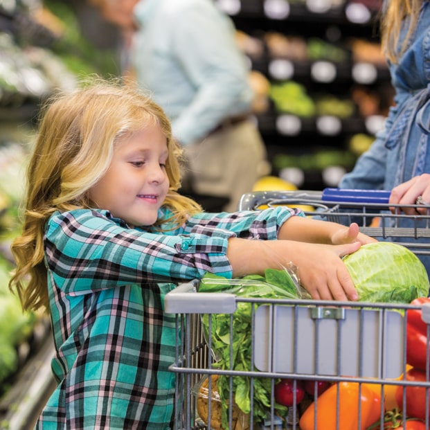 Child putting vegetables in grocery cart